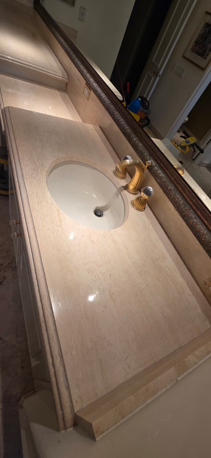 Polished beige natural stone bathroom vanity with an undermount sink and gold faucet.