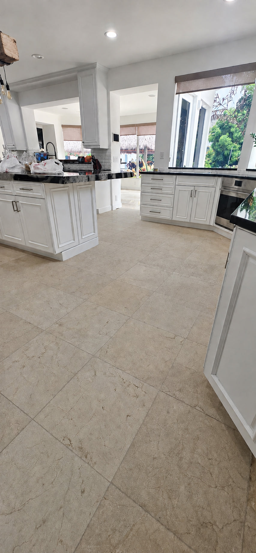 Cream marble tile kitchen floor before final polishing, with the surrounding white cabinetry protected during restoration.